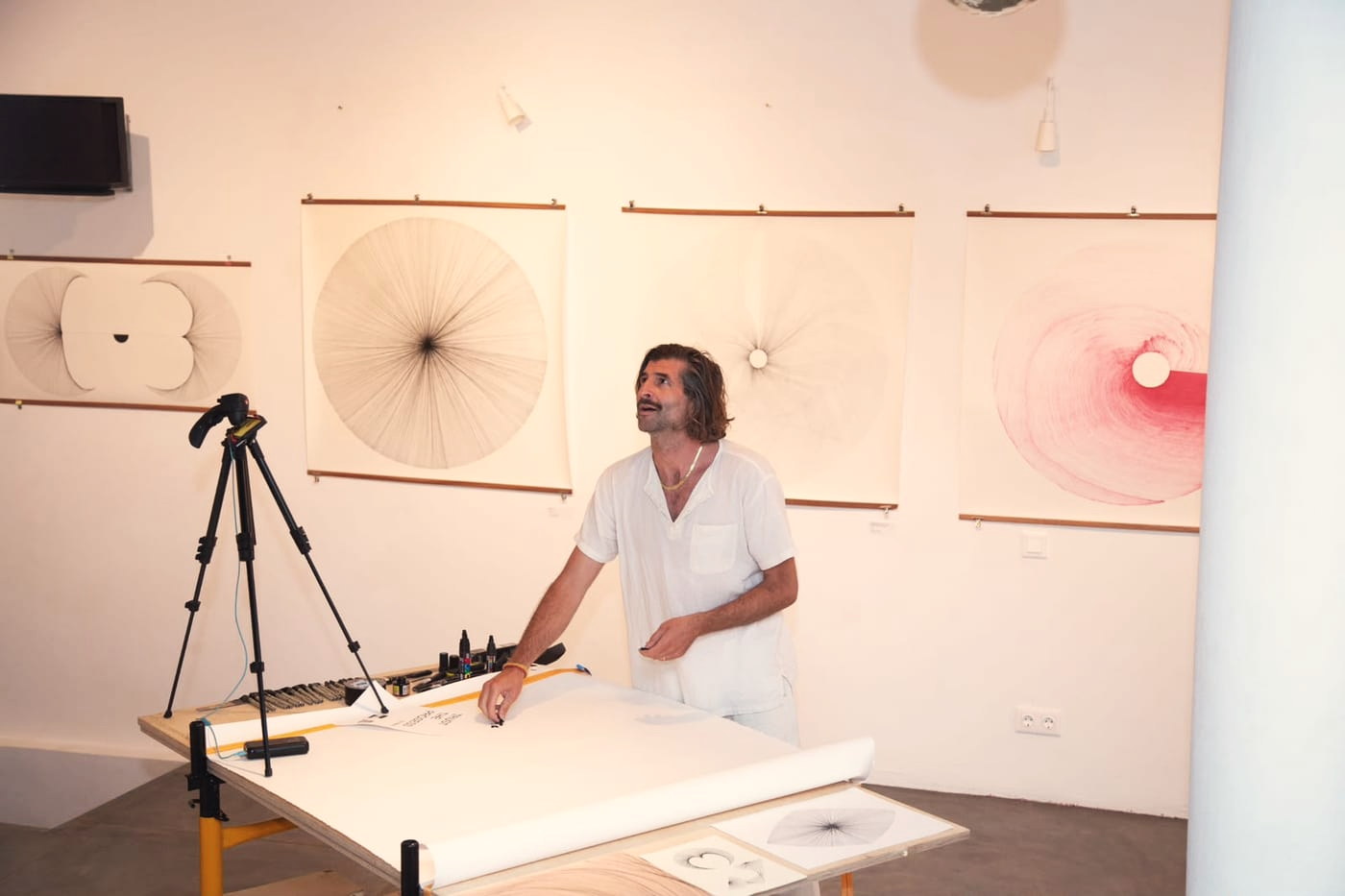 Mischa é Volve at his drawing table, his radial line drawings hung on the wall behind him