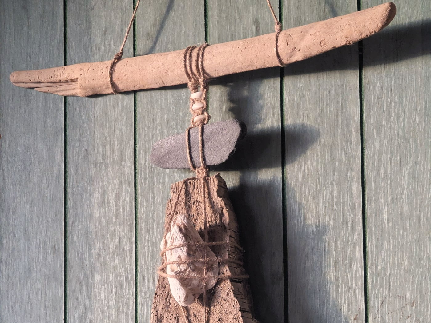 A driftwood wall hanging by Philine Allard: a stone and a shell bound in jute to a weathered bar